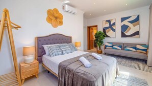 A bedroom with a bed, bedside table, lamp, air conditioning unit, and abstract wall art. - Villa Casa Luna by Villa Plus (Playa Blanca)