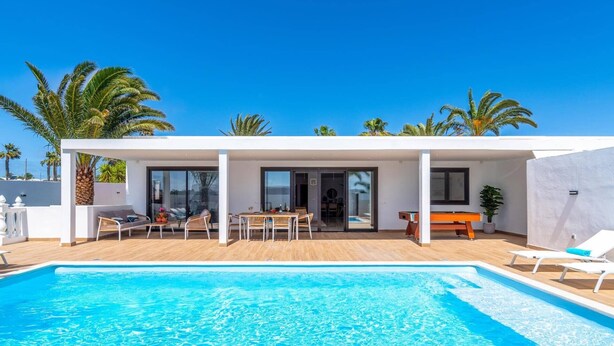 A modern house with a swimming pool, outdoor seating, and palm trees. - Villa Casa Luna by Villa Plus (Playa Blanca)
