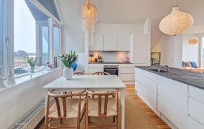Een moderne keuken met witte kasten, een eettafel met stoelen en hanglampen.