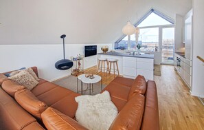 Een modern loft appartement met een open keuken in loftstijl, een groot raam met uitzicht, een bruine leren bank en een kleine ronde tafel.