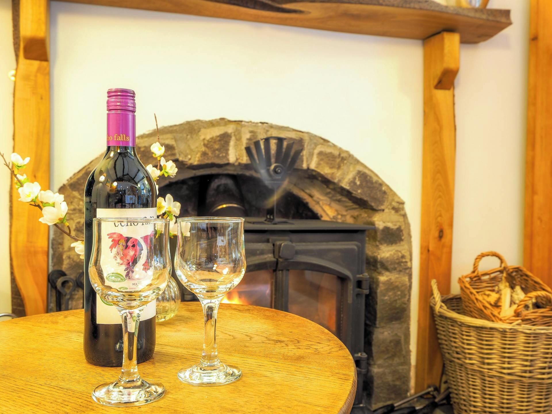 A bottle of wine, two glasses, and a fireplace in a rustic setting.
