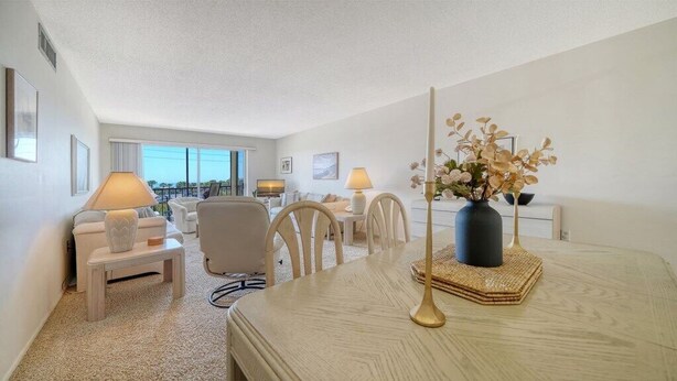 A hotel room with a bed, a desk, two chairs, a lamp, a vase with flowers, and a view of the outdoors. - Siesta Key Beach Unit 306 (Sarasota)