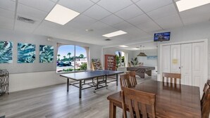 A spacious room with a ping pong table, wooden chairs, a large window with a view, and artwork on the walls. - Siesta Key Beach Unit 306 (Sarasota)