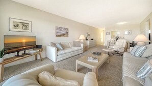 A spacious living room with a large flat-screen TV, a sofa, a chair, and a coffee table. - Siesta Key Beach Unit 306 (Sarasota)