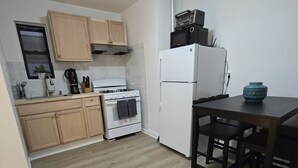 A compact kitchen with a stove, oven, and refrigerator, wooden cabinets, and a dining table with chairs. - Simple, Quiet & Clean w/ Workstations (New York)