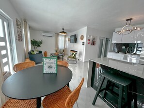 Eine moderne Küche mit Kochinsel, Essbereich mit Korbstühlen und Wohnbereich mit Sofa und Pflanzen.