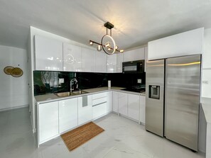 Eine moderne Küche mit weißen Schränken, einem Edelstahl-Kühlschrank, einer schwarzen Arbeitsplatte und einer außergewöhnlichen Deckenleuchte.