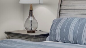 Een bed met een gestreept kussen, een nachtkastje met een lamp en een houten hoofdbord.