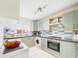 Een moderne keuken met een gasfornuis, oven, wasmachine en een schaal fruit op het aanrecht.