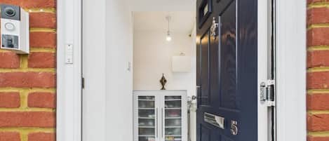 Un couloir avec une porte bleu foncé, un meuble blanc aux portes vitrées et une caméra de surveillance fixée au mur.