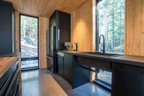 A modern kitchen with a large window, built-in appliances, and a view of the forest. - Spa and Escape by the Water | Loveshack (Saint-Alphonse-Rodriguez)