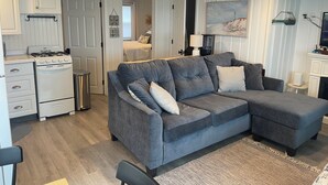 A modern living room with a grey sectional sofa, a white stove, and a painting on the wall. - Cozy 2-bedroom condo located directly on Hampton Beach with AC (Hampton)