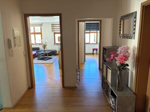 Un couloir avec un plancher en bois, un canapé, une table à manger et un vase rempli de fleurs.