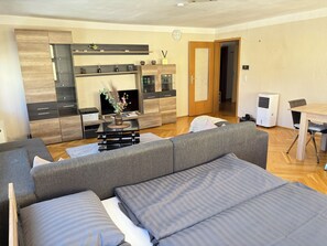 Un salon moderne comprenant un canapé, un téléviseur, un meuble en bois et un coin repas avec une table et des chaises.