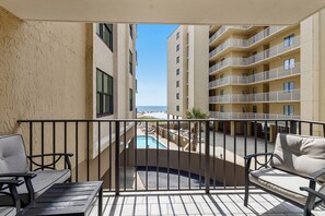 Un balcón con piscina, mobiliario exterior y vista a un edificio y una playa.