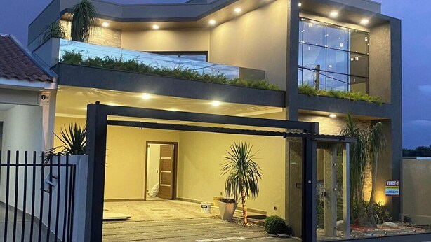 Une maison moderne à deux étages, dotée d’une entrée sécurisée par un portail, d’un balcon et d’une grande fenêtre à l’étage supérieur.