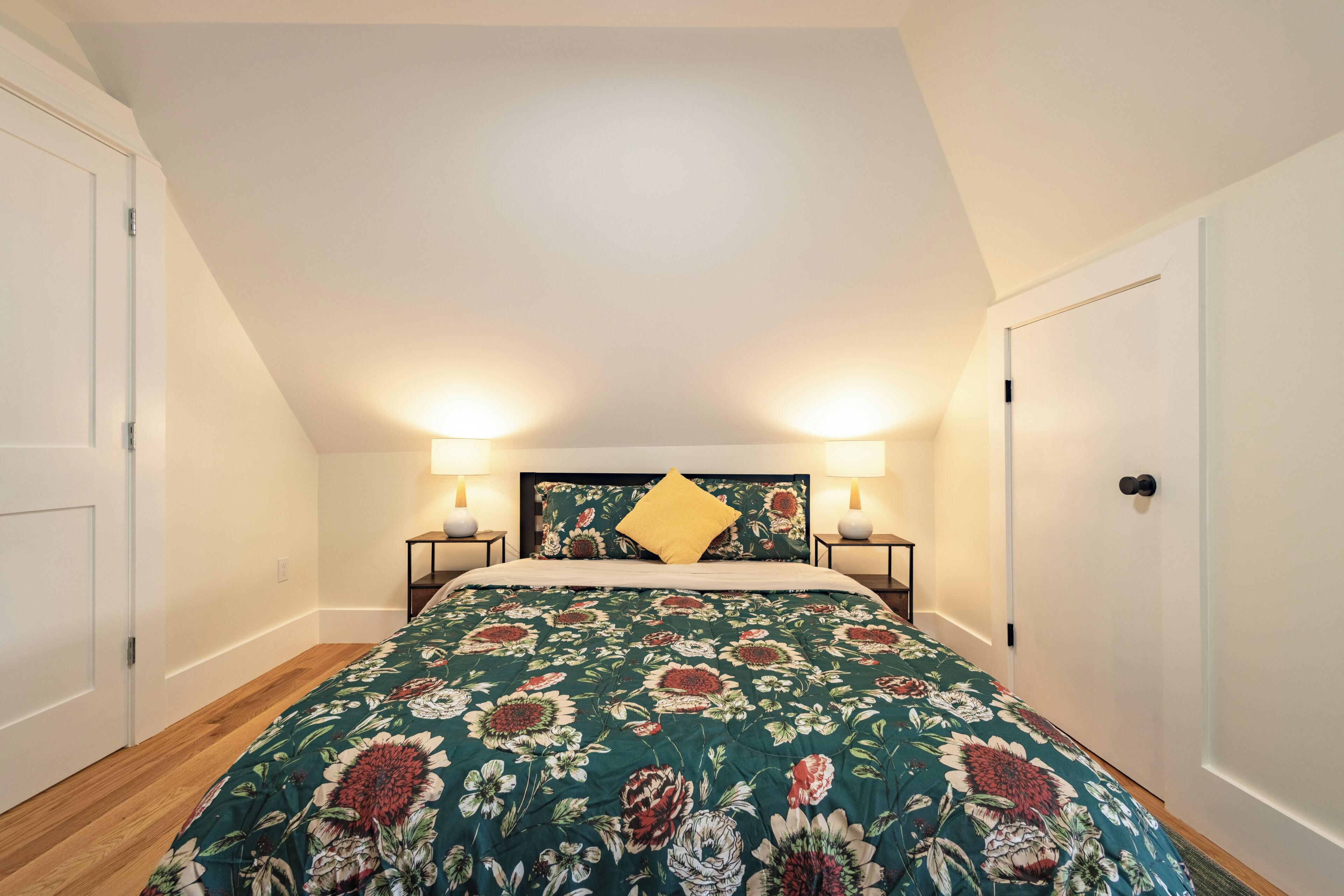 A bedroom with a floral bedspread, two bedside lamps, and a wooden floor.