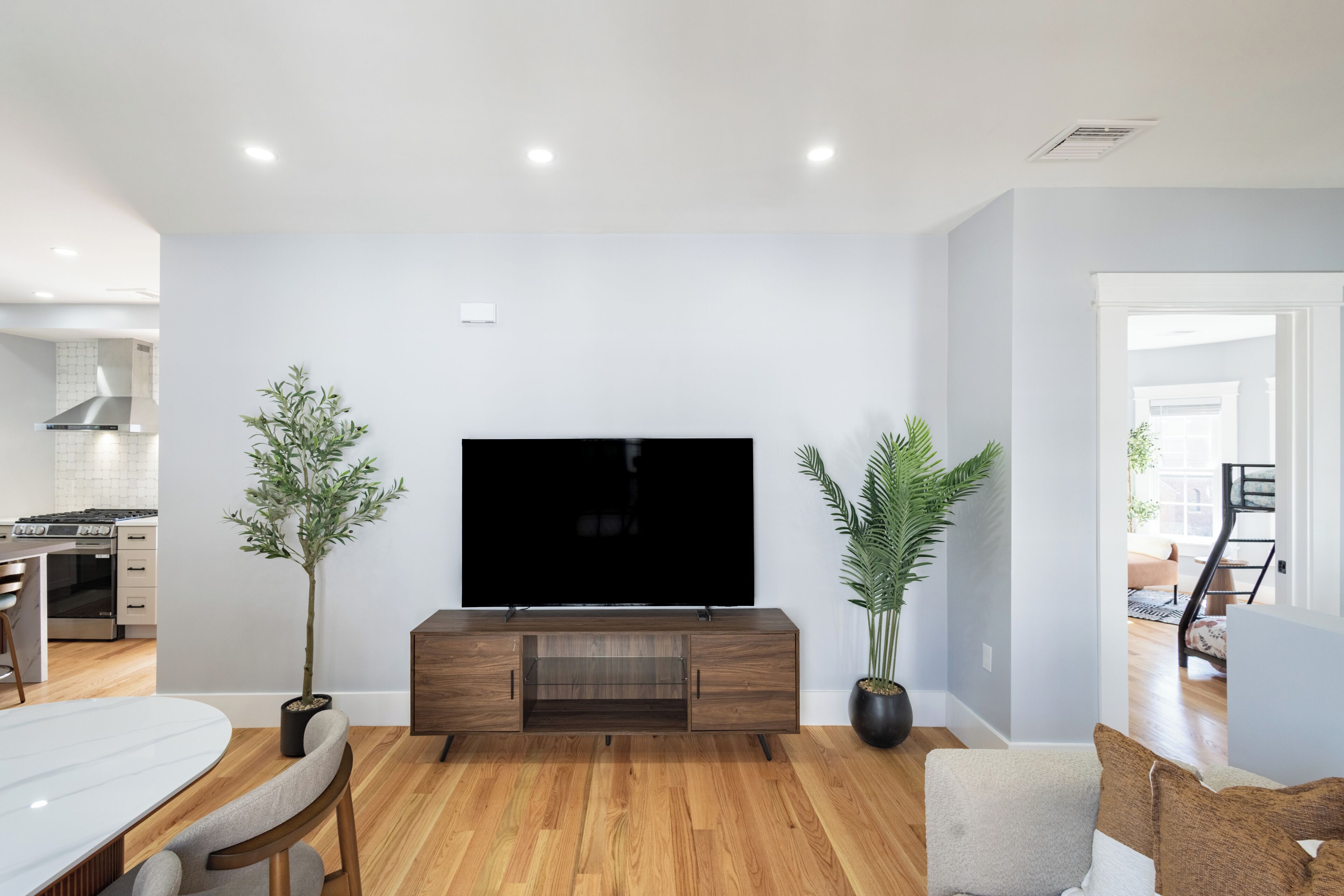 A modern living room with a flat-screen TV, wooden flooring, and a dining area with a white table and chairs.