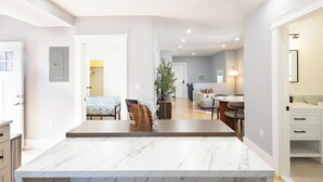 A modern kitchen with a marble countertop, a dining area with a table and chairs, and a living space with a sofa and a plant. - Stunning 4BR2BA w Parking/Near Downtown/ +Parking (Boston)
