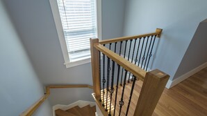 A wooden staircase with black balusters, a window with blinds, and a light blue wall. - Stunning 4BR2BA w Parking/Near Downtown/ +Parking (Boston)