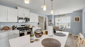 Une cuisine moderne avec des meubles blancs, des appareils en acier inoxydable et un coin repas comprenant une table et des chaises.