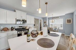 A modern kitchen with white cabinets, stainless steel appliances, and a dining area with a table and chairs. - Premium Penn State Home • Sleeps 13 • Allen Street (State College)