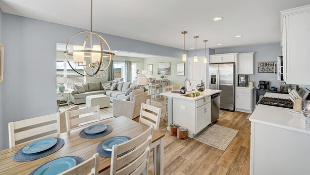Une cuisine moderne avec des meubles blancs, un îlot central et un coin repas comprenant une table en bois et de l’assiette bleue.