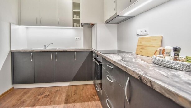 A modern kitchen with dark cabinets, a marble countertop, and a wooden cutting board.
