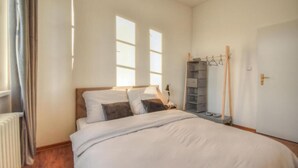 A bedroom with a bed, a nightstand, a radiator, a window, and a door.