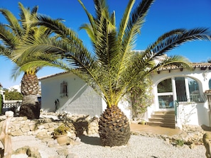 A building with a stone wall, palm trees, and a white facade.