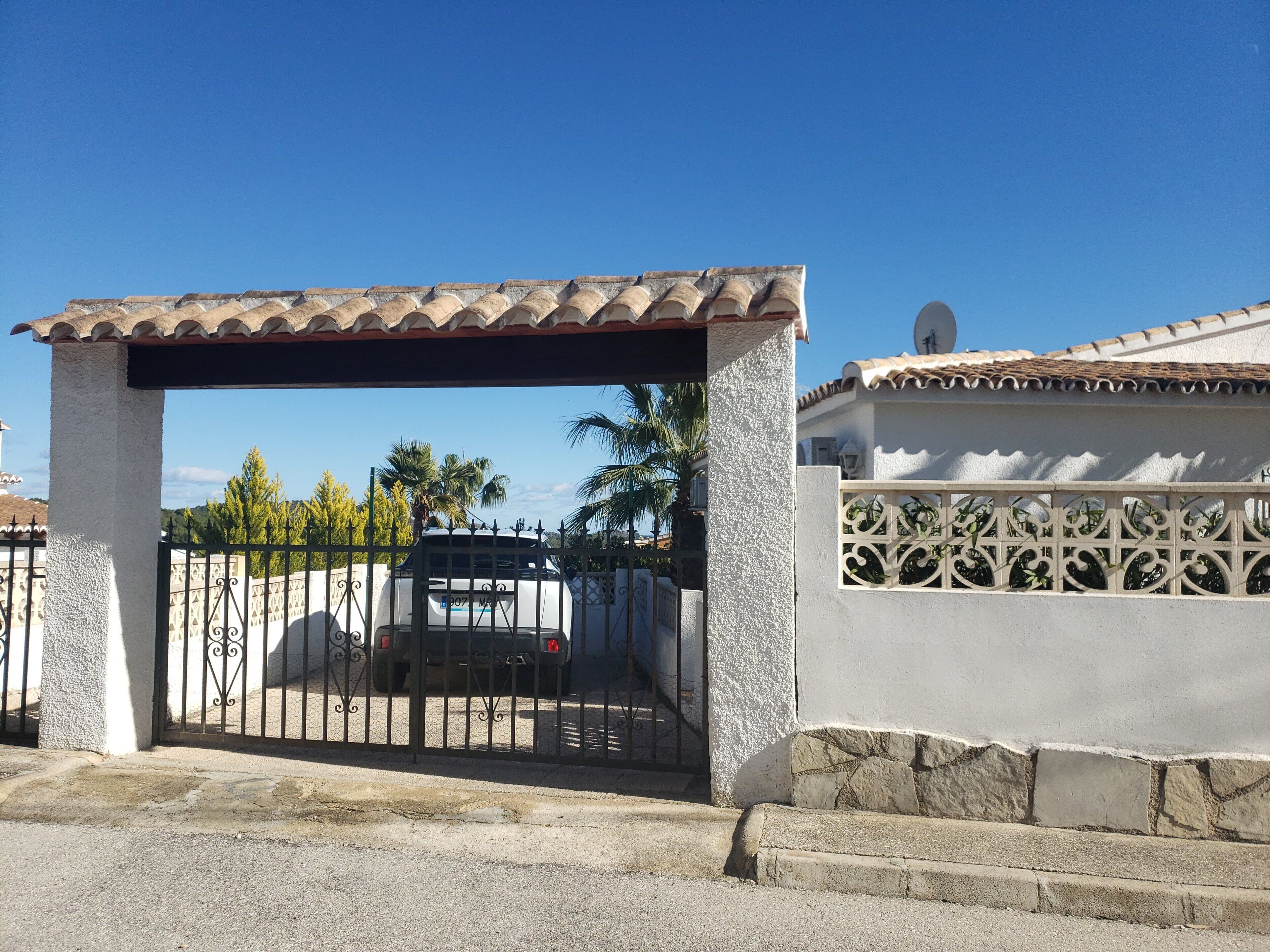 A gated entrance with a tiled roof, a white wall with decorative patterns, and a parked vehicle in the background.