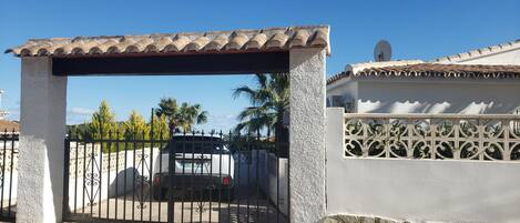 A gated entrance with a tiled roof, a white wall with decorative patterns, and a parked vehicle in the background.
