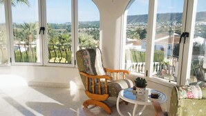 A room with large arched windows, a wooden ceiling, a green upholstered sofa, a wooden chair, and a small round table with a potted plant. - Villa Mitica with Private Pool in Benitachell (El Poble Nou de Benitatxell/Benitachell)