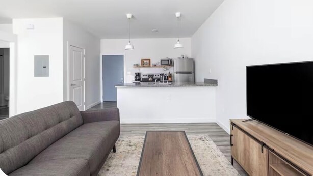 A modern living room with a sofa, a coffee table, a TV, and a kitchen area with appliances.
