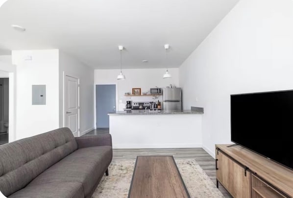 A modern living room with a sofa, a coffee table, a TV, and a kitchen area with appliances.