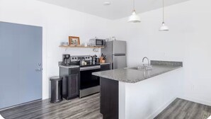 A modern kitchen with a built-in oven, microwave, and refrigerator, a granite countertop, and pendant lighting.