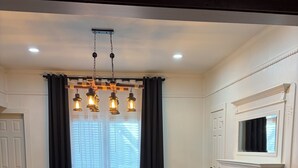 A dining room with a long table, black chairs, a black rug, a fireplace, and a TV mounted above it. - The Corner 82 /High End Nature Escape King beds (Winder)