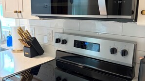A kitchen with a stainless steel microwave, oven, and a digital clock displaying 3:57. - The Corner 82 /High End Nature Escape King beds (Winder)