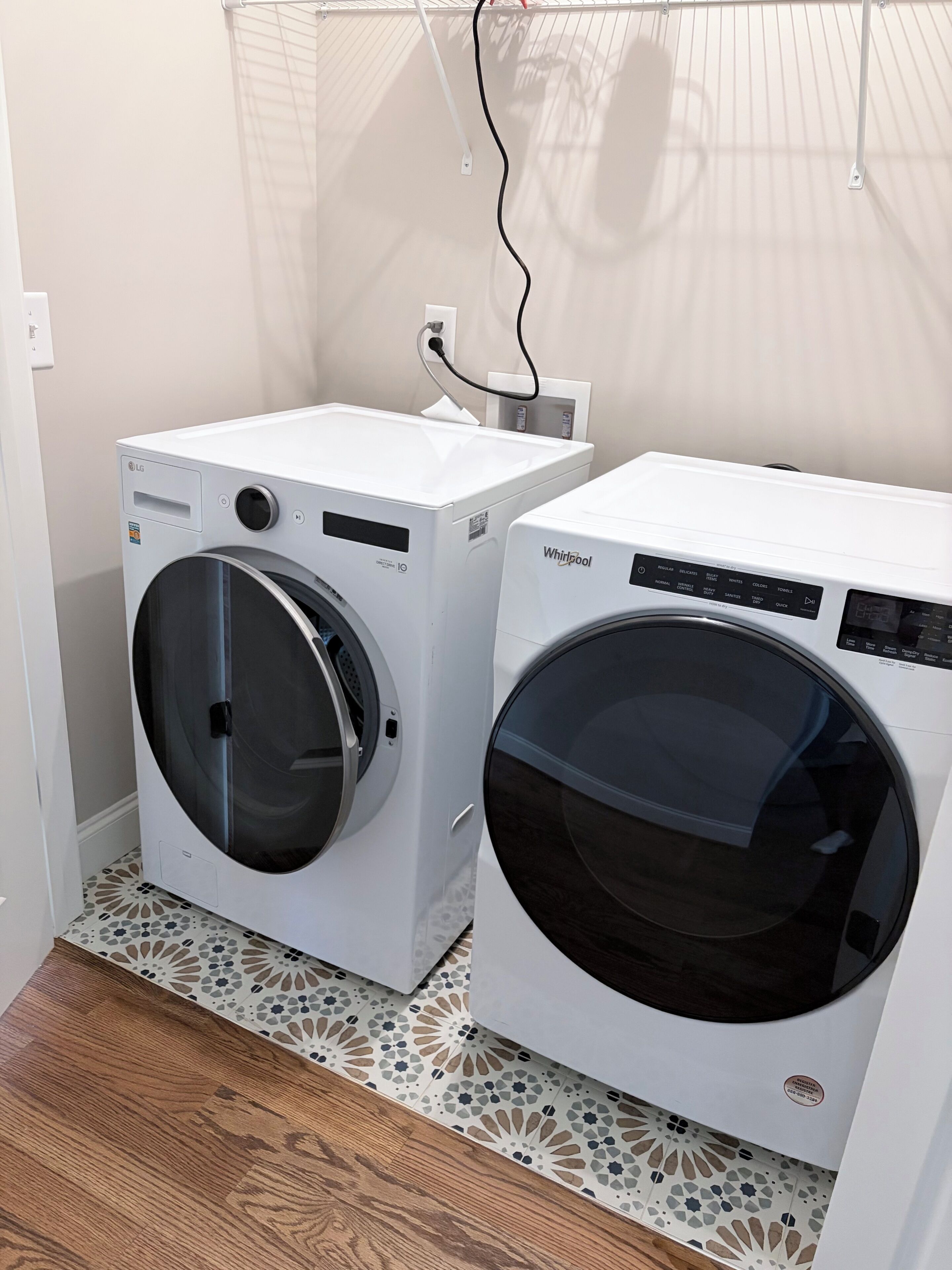 Two front-loading washing machines in a laundry room with patterned floor tiles and a power outlet on the wall.