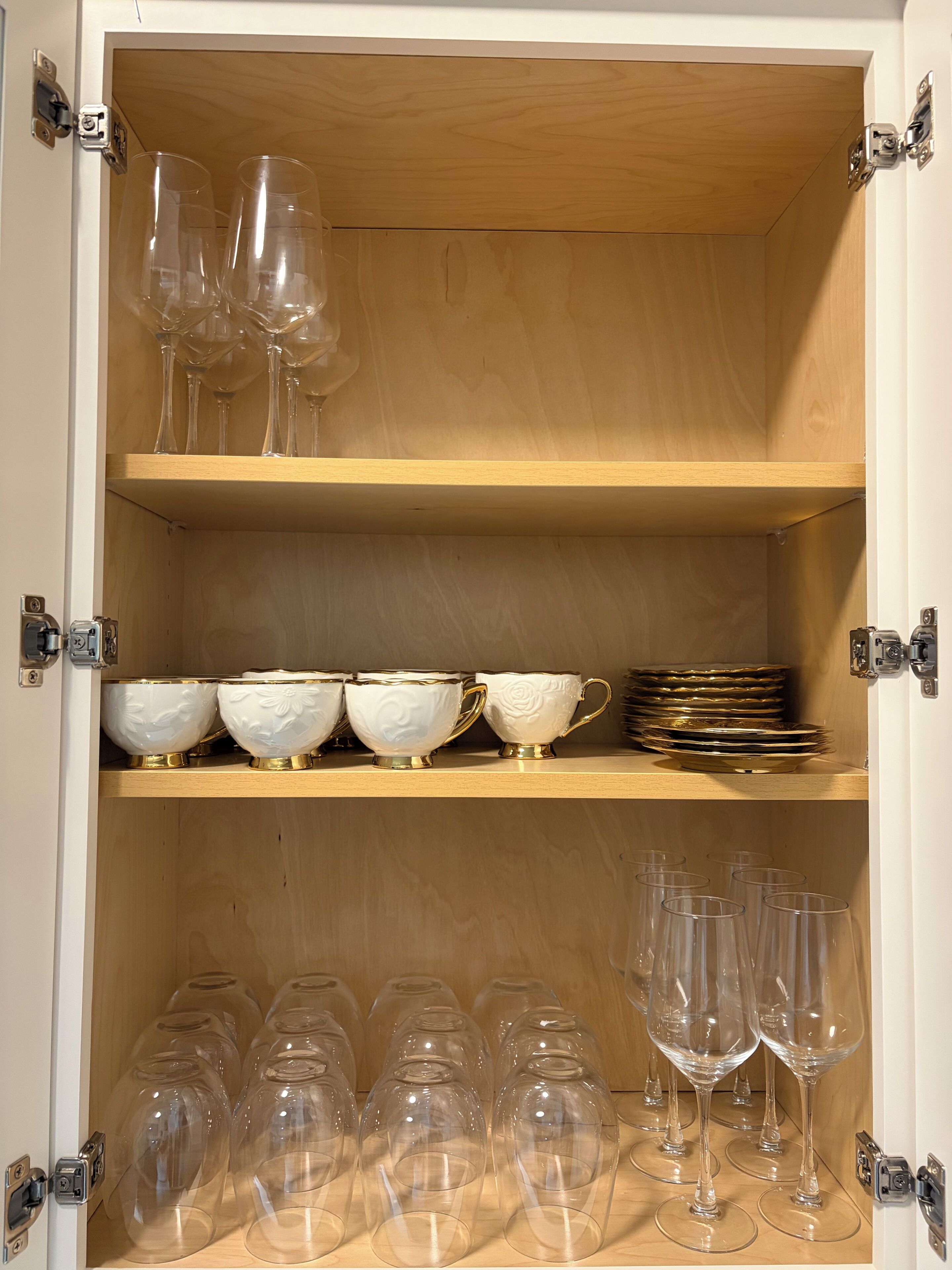 Un meuble avec trois étagères, chacune contenant différents objets : l’étagère du haut est réservée aux verres à vin, l’étagère du milieu contient des bols et des assiettes, et l’étagère du bas contient d’autres verres à vin.