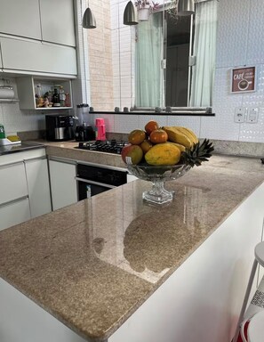 Eine Küche mit einer Arbeitsplatte aus Granit, einer Obstschale, einer Kaffeemaschine und einem Fenster mit Aussicht.