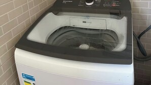 A front-loading washing machine in a laundry room with a shelf above containing cleaning supplies. - Cozy apartment in Belém, close to the main tourist attractions. (Belém)