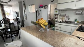 A modern kitchen with white cabinets, a granite countertop, a dining area with a glass table, and a red rug. - Cozy apartment in Belém, close to the main tourist attractions. (Belém)