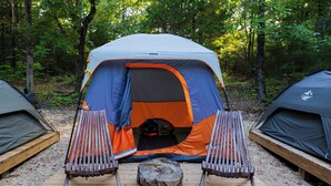 Montagem para camping com uma tenda, duas cadeiras e um tronco.