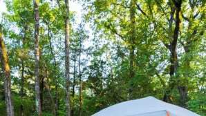 Montagem de camping com uma tenda, duas cadeiras e uma mesa de madeira em um deck.