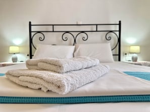 Una cama bien tendida con sábanas blancas y un detalle en color turquesa, un cabecero de metal negro y dos lámparas de noche.