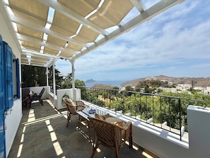 A covered outdoor seating area with a view of the sea and hills. - Villa Fenia (Amorgos)
