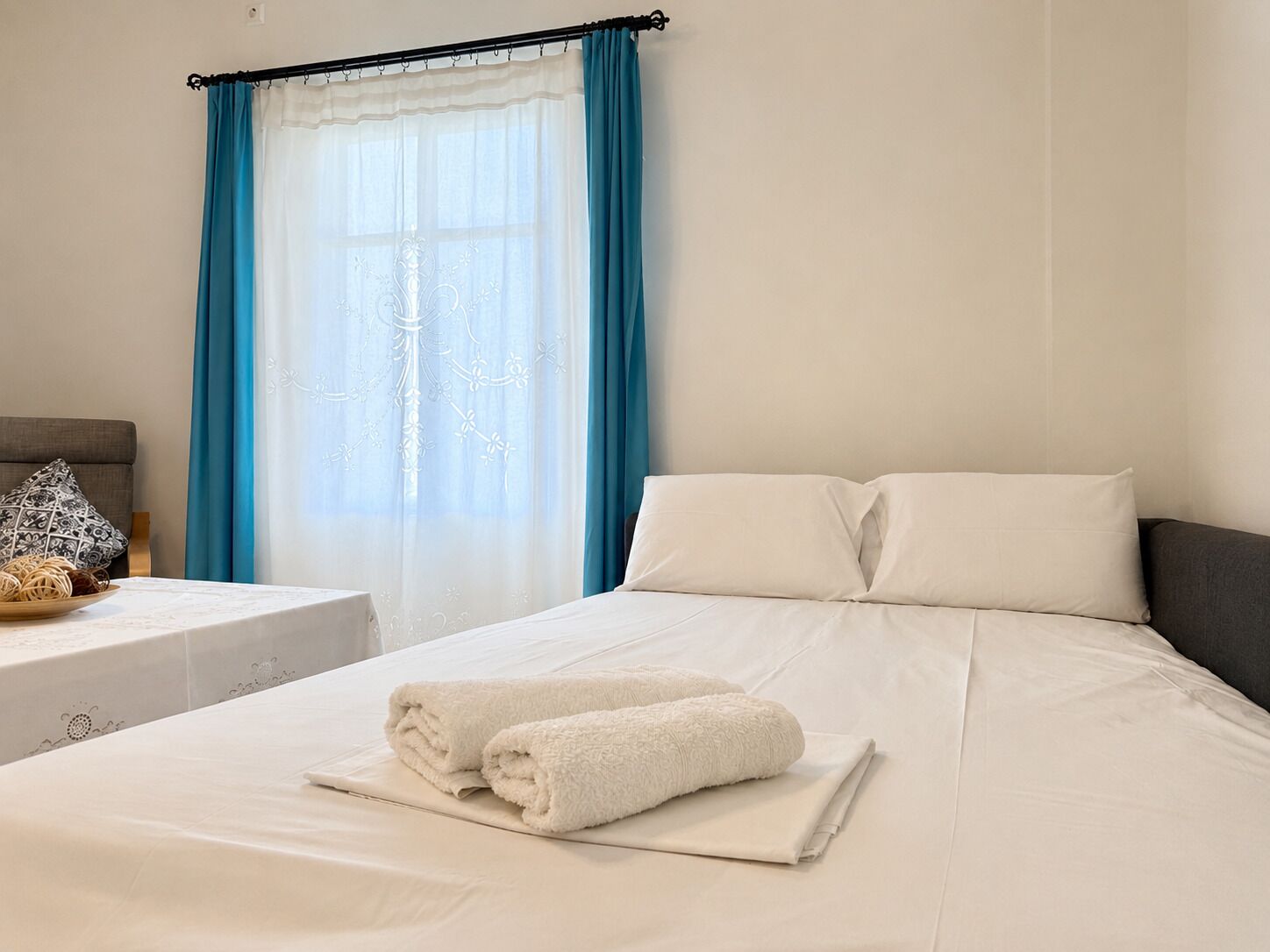 Una habitación de hotel con una cama, una mesita de noche con un frutero, y una ventana con cortinas azules.