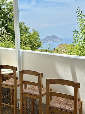 A balcony with wooden chairs and a view of the sea and a mountain. - Villa Fenia (Amorgos)