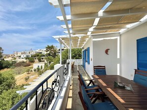 A balcony with a wooden table and chairs, a white railing, and a view of houses in the distance. - Villa Fenia (Amorgos)